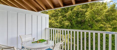 A balcony with a white railing, a round table with chairs, and a view of dense green foliage.