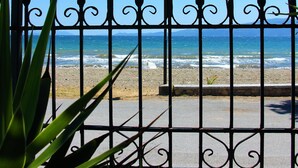 Ein Metallzaun mit Verzierungen, der zu einem Strand mit dem Meer im Hintergrund führt.