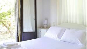 Ein Schlafzimmer mit Holzbalkendecke, einem Bett mit weißer Bettwäsche, einem Nachttisch mit Lampe und einem Fenster mit Vorhängen.