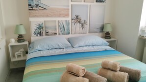 Een slaapkamer met een bed, kussens, een gestreepte dekbedovertrek en handdoeken.