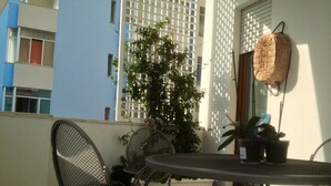 Een balkon met een ronde tafel, twee stoelen, plantenbakken en een rieten mand.