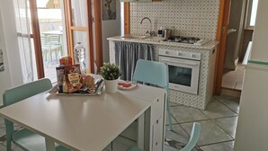 Een compacte keuken met een eethoek, voorzien van een klein fornuis, wastafel en een potplant op de tafel.