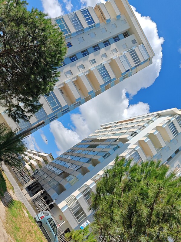 A high-rise building with multiple balconies, large windows, and a clear sky with clouds.