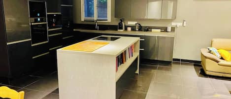 Una cocina moderna con una isla central, electrodomésticos integrados y un área de comedor con una silla.