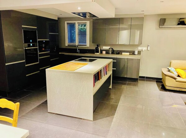 A modern kitchen with a central island, built-in appliances, and a dining area with a yellow chair. - Very nice 80 m2 apartment (Pianottoli-Caldarello)