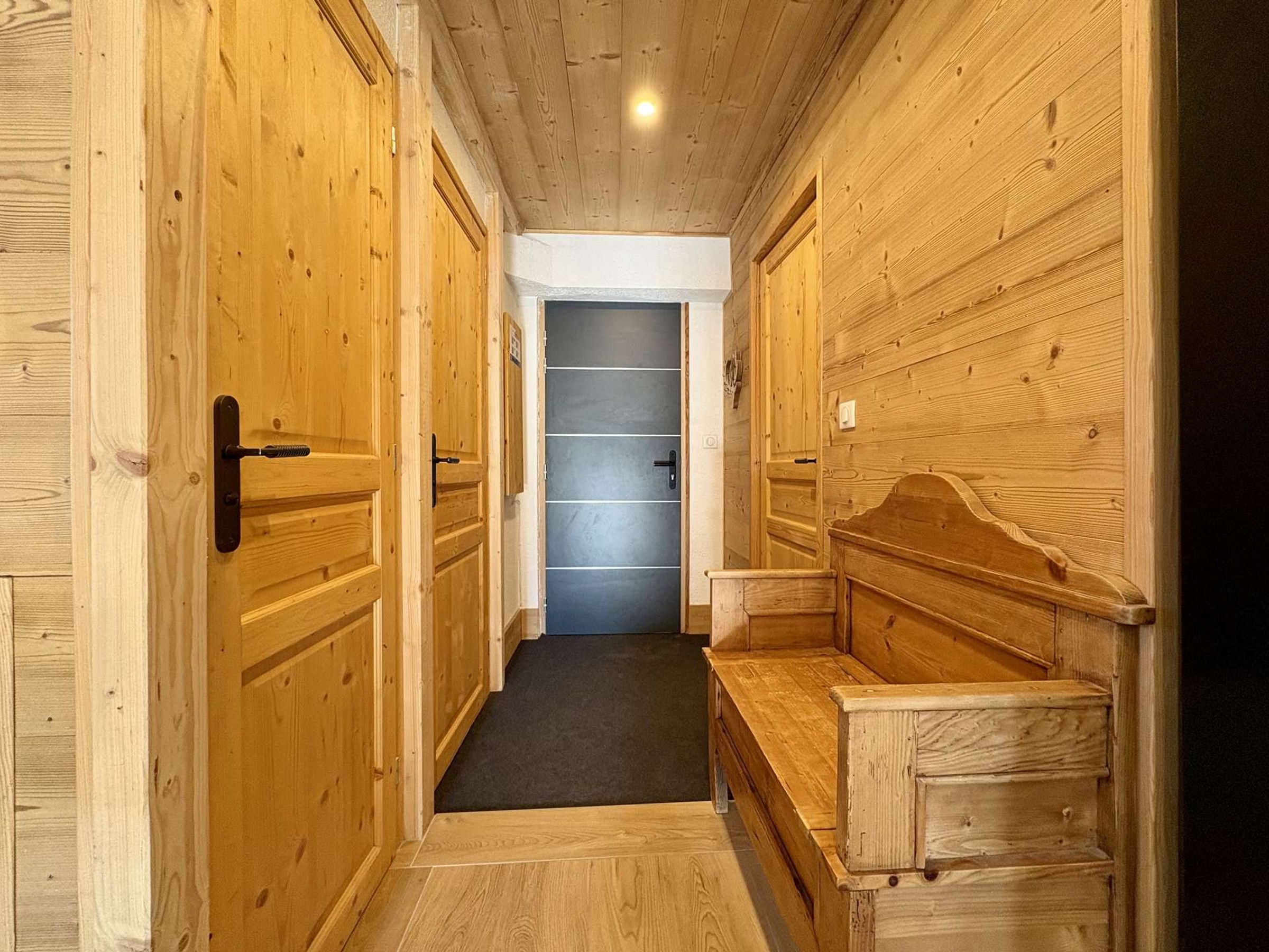 A hallway with wooden walls and doors, a bench, and a dark-colored door at the end.