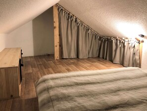 A bedroom with a sloped ceiling, wooden flooring, a bed with a grey blanket, and curtains with bows. - 4-room apartment for 10/12 people in Briançon with Wifi (Briançon)