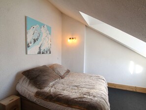 A bedroom with a bed, a painting of mountains, a wall-mounted light, and a sloped ceiling. - 4-room apartment for 10/12 people in Briançon with Wifi (Briançon)