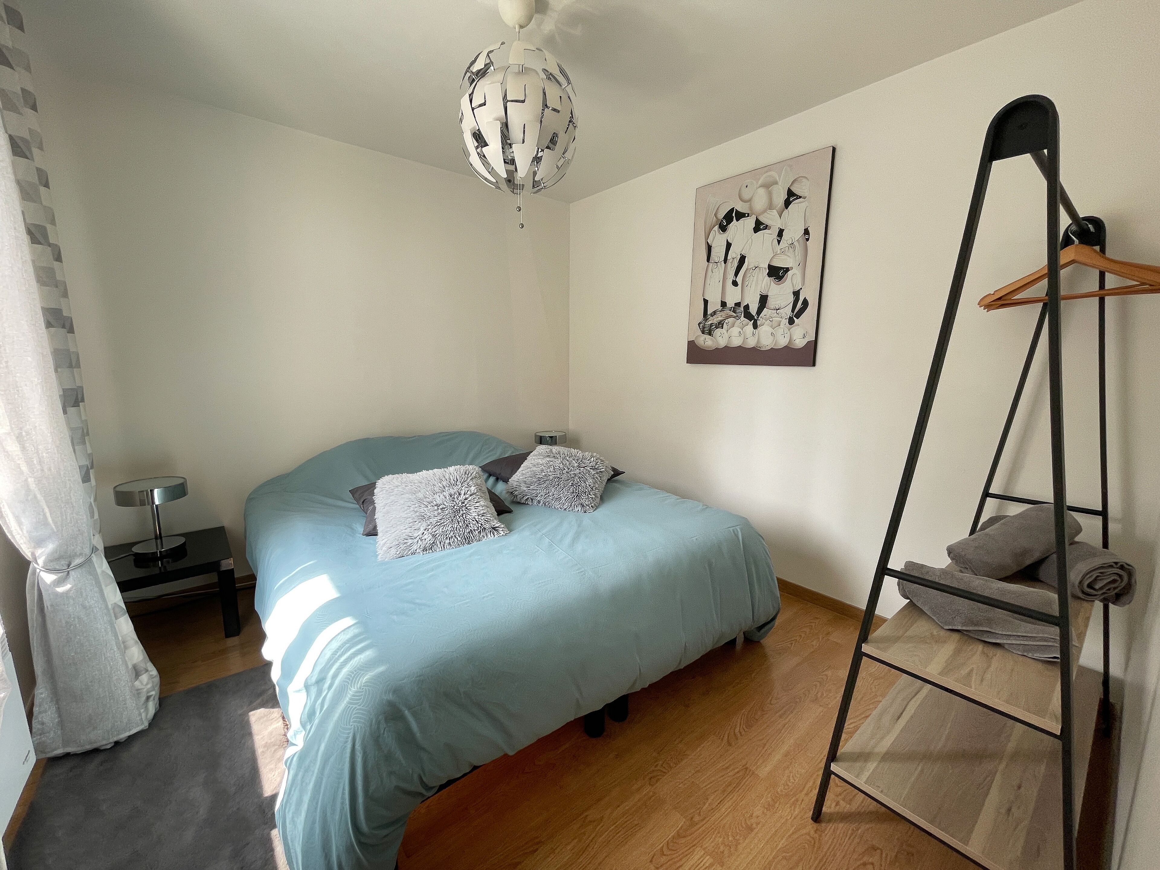 Une chambre à coucher avec un lit, un luminaire suspendu, un tableau et un plancher en bois.