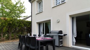Un espace extérieur aménagé pour les repas, avec une table dressée pour six personnes, entourée de chaises, et un barbecue.