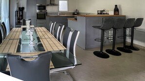 Une cuisine moderne avec un coin repas. Elle comprend un îlot de cuisine avec des tabourets, une table à manger avec des chaises et des appareils électroménagers intégrés.