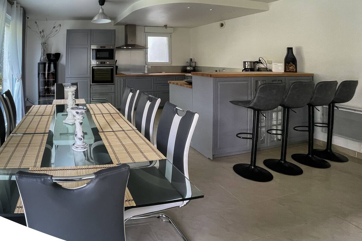 Una cocina moderna con comedor. Cuenta con una isla de cocina con taburetes, una mesa de comedor con sillas y electrodomésticos integrados.