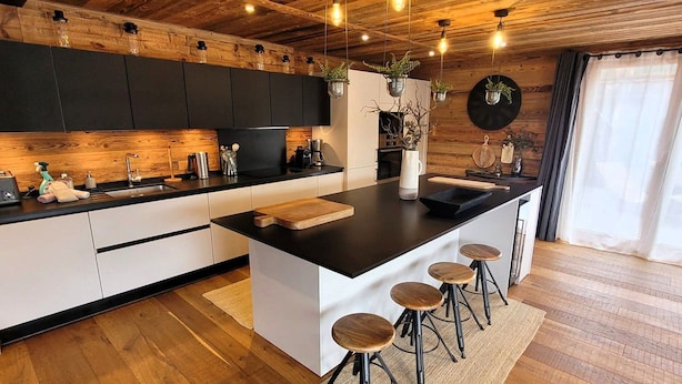 A modern kitchen with a central island, bar stools, wooden flooring, and a rustic ceiling. - Spacious 5* chalet with jacuzzi and sauna, pets allowed (Les Gets)