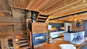 A modern kitchen with a central island, wooden staircase, and a cozy seating area with two chairs. - Spacious 5* chalet with jacuzzi and sauna, pets allowed (Les Gets)