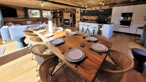 A modern kitchen with white cabinets, a central island, and a dining area with a wooden table and wicker chairs. - Spacious 5* chalet with jacuzzi and sauna, pets allowed (Les Gets)