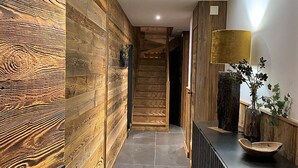 A modern interior with wooden paneling, a black console table with a vase and bowl, and a staircase leading to another room. - Spacious 5* chalet with jacuzzi and sauna, pets allowed (Les Gets)