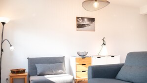 Ein modernes Wohnzimmer mit grauem Sofa, einem Holznachttisch, einem weißen Schrank mit Schubladen und einer hängenden Leuchte.