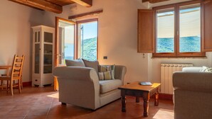 A cozy living room with a sofa, a wooden table, and a view of a mountainous landscape through a window. - Family Friendly Accommodation in Umbria (Perugia)
