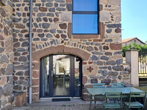 A stone building with a large arched doorway, a window, and a table with chairs outside. - Charming Mountain Retreat: Cozy Gîte with Modern Amenities, Scenic Trails & Stargazing Opportunities (Le Vernet)