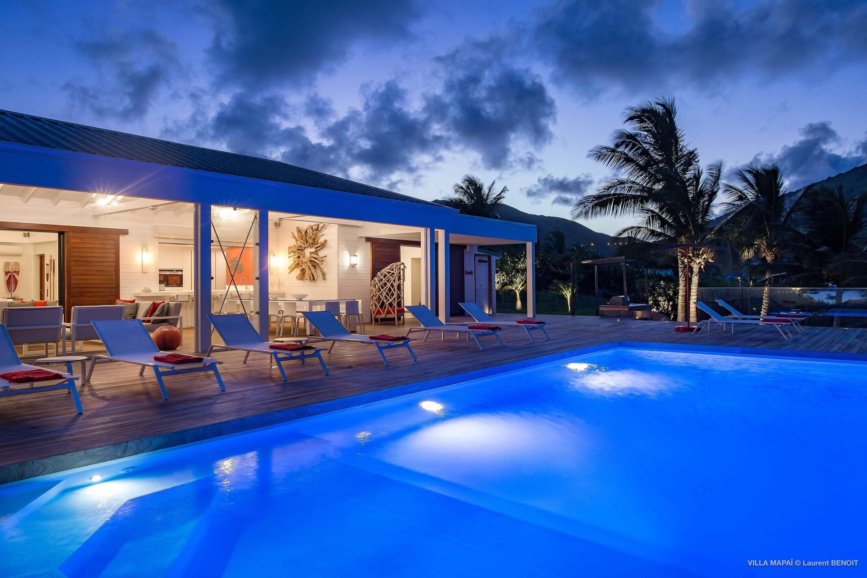 Ein moderner Poolbereich mit Liegestühlen und einem Pool, umgeben von einer Holzterrasse und Palmen.
