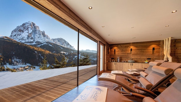 A modern room with a large window overlooking a snowy mountain. There are several reclining chairs and a wooden table with menus.