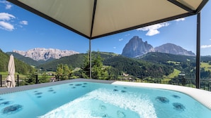 A hot tub with a mountain view, surrounded by a covered area with a railing.