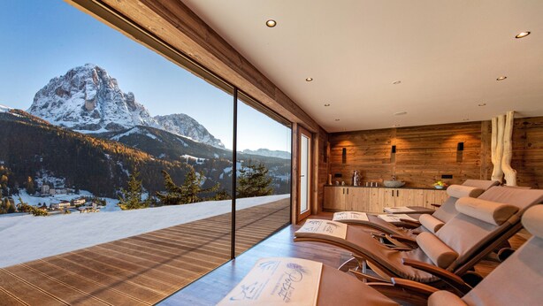 Une pièce moderne dotée d’une grande fenêtre donnant sur une montagne enneigée. On y trouve plusieurs fauteuils inclinables et une table en bois avec des menus.