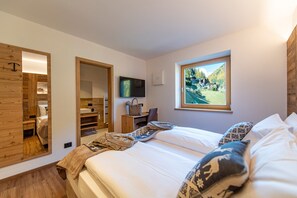 Een slaapkamer met een bed, een televisie, een bureau en een raam met uitzicht op een berglandschap.