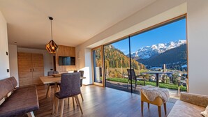 Un salon moderne avec un coin repas en bois et une grande porte-fenêtre coulissante donnant sur un balcon avec vue sur les montagnes.