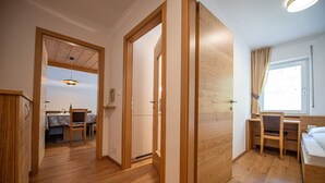 Een hotelkamer met een houten vloer, een bed, een bureau en een stoel. Door een open deur is een zithoek zichtbaar.