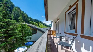 Een balkon met een houten terras, twee metalen stoelen en een tafel.