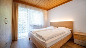Een slaapkamer met een houten bed, nachtkastje, kledingkast en een raam met gordijnen.