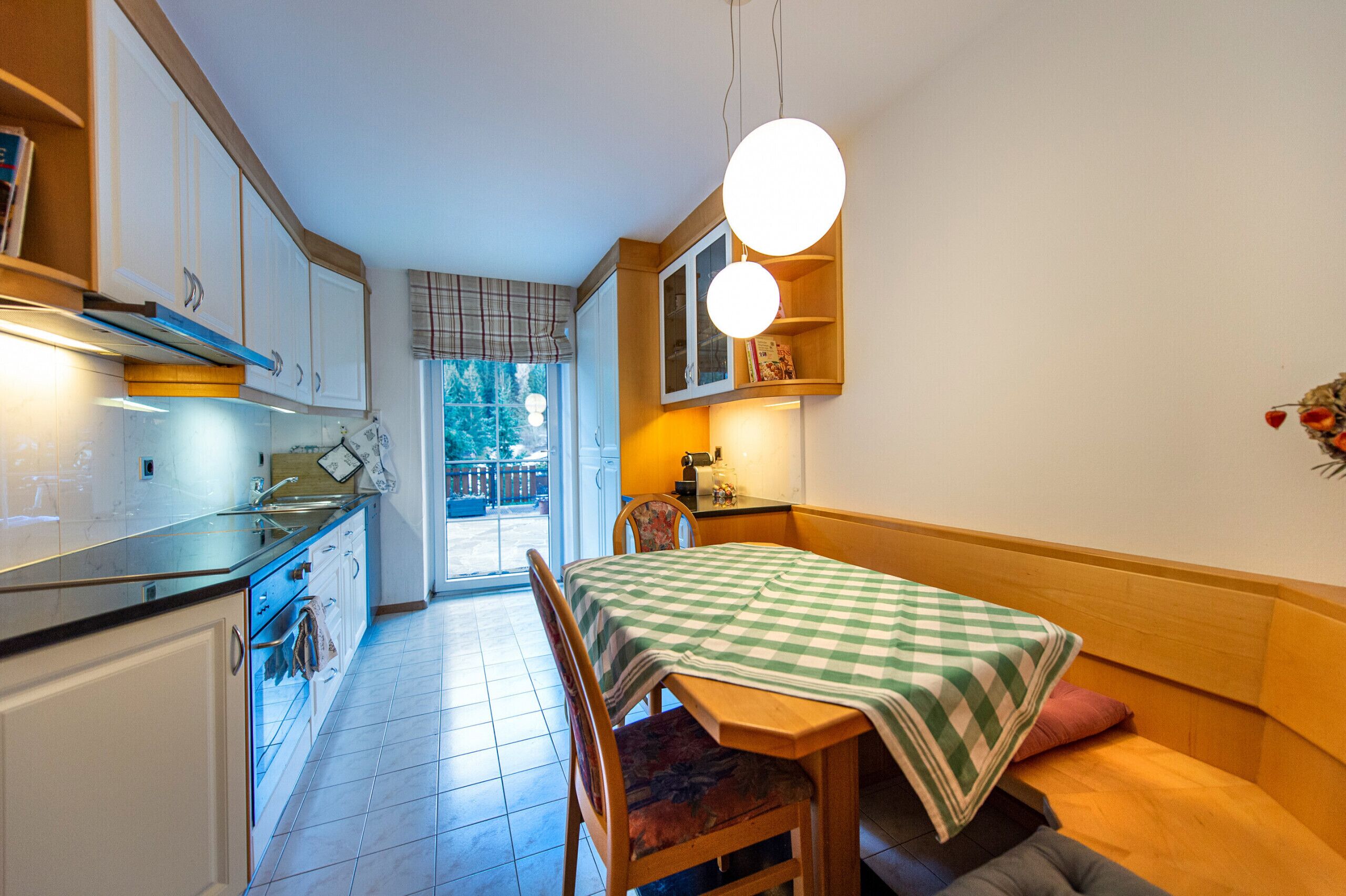 A kitchen with white cabinets, a wooden table with a checkered tablecloth, and a dining chair.