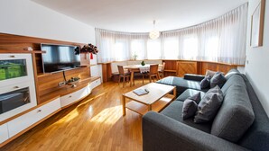 Un salon moderne doté d’un téléviseur à écran plat, de meubles en bois, d’un canapé gris et d’un coin repas avec une table et des chaises.