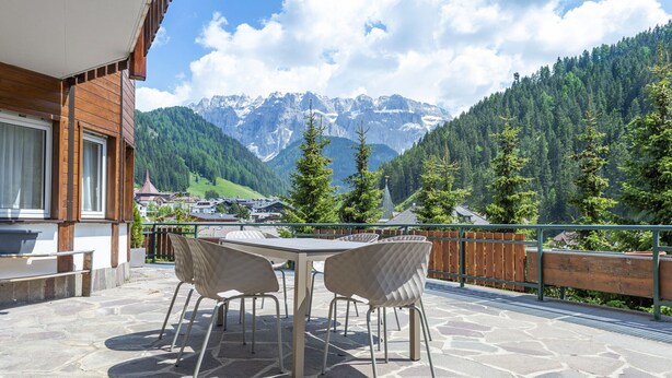 Une terrasse extérieure avec une table et des chaises, une clôture en bois et une vue sur les montagnes et la forêt.