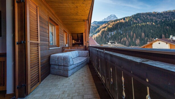 Un balcon en bois avec un canapé, une balustrade en bois et une vue sur une montagne et une forêt.