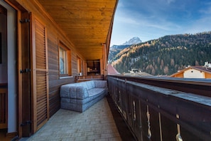 Un balcon en bois avec un canapé, une balustrade en bois et une vue sur une montagne et une forêt.