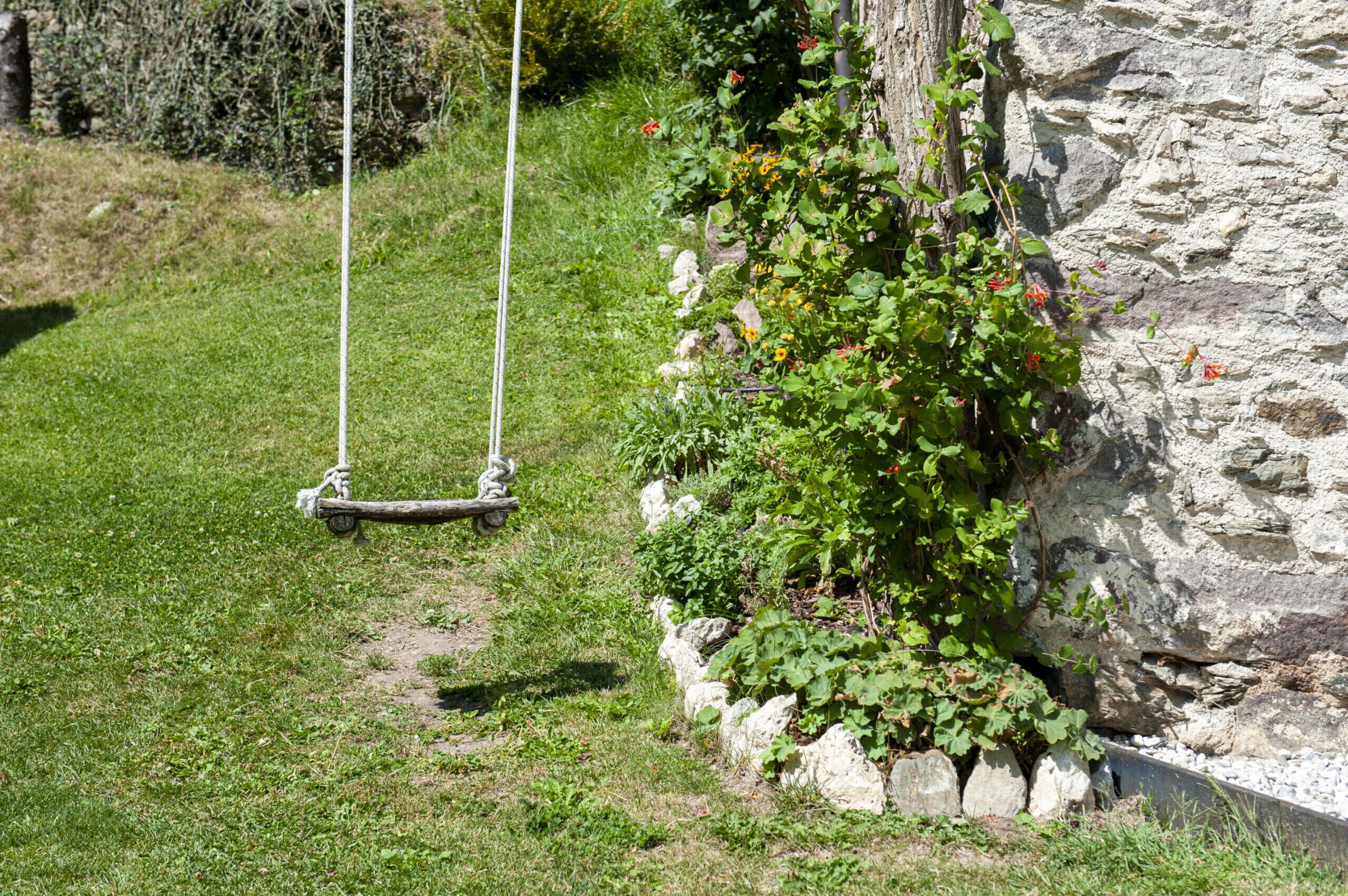 A garden with a swing set, a stone wall, and greenery.