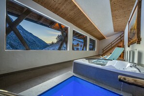 Ein modernes Badezimmer mit einer großen Badewanne, einer Holzbalkendecke und großen Fenstern mit Blick auf eine verschneite Landschaft.