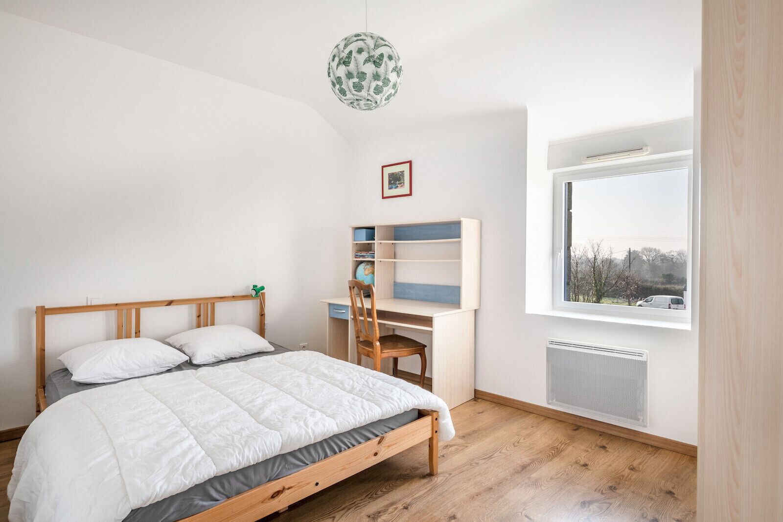 Une chambre à coucher avec un lit en bois, un bureau avec une chaise, un globe terrestre et une fenêtre donnant sur l’extérieur.
