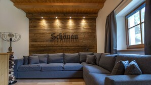 A modern living room with a wooden wall, a grey sectional sofa, and a window with curtains.