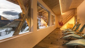 A room with large windows, wooden flooring, and a view of a snowy landscape.