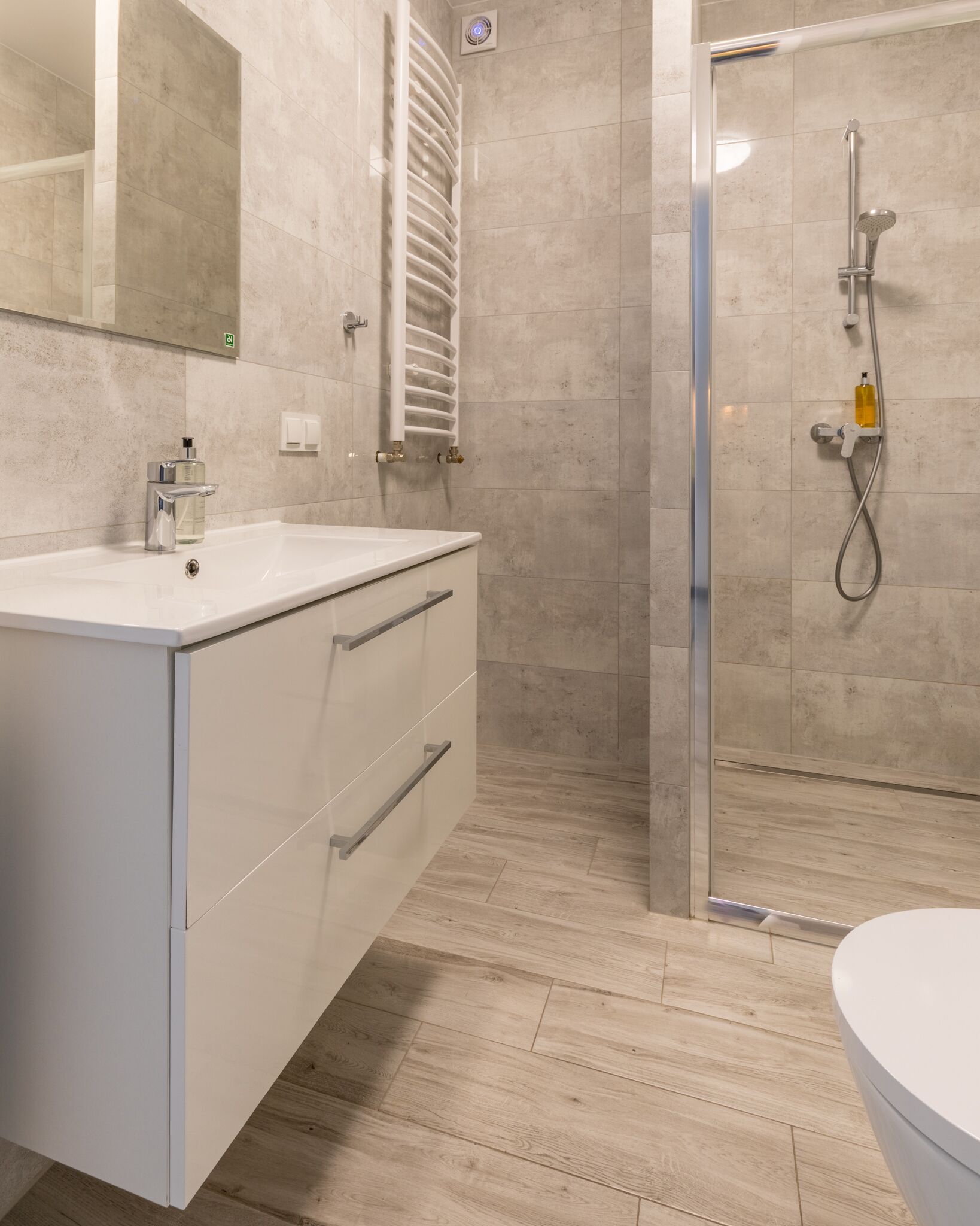 A modern bathroom with a white vanity, a glass shower enclosure, and a wooden floor.