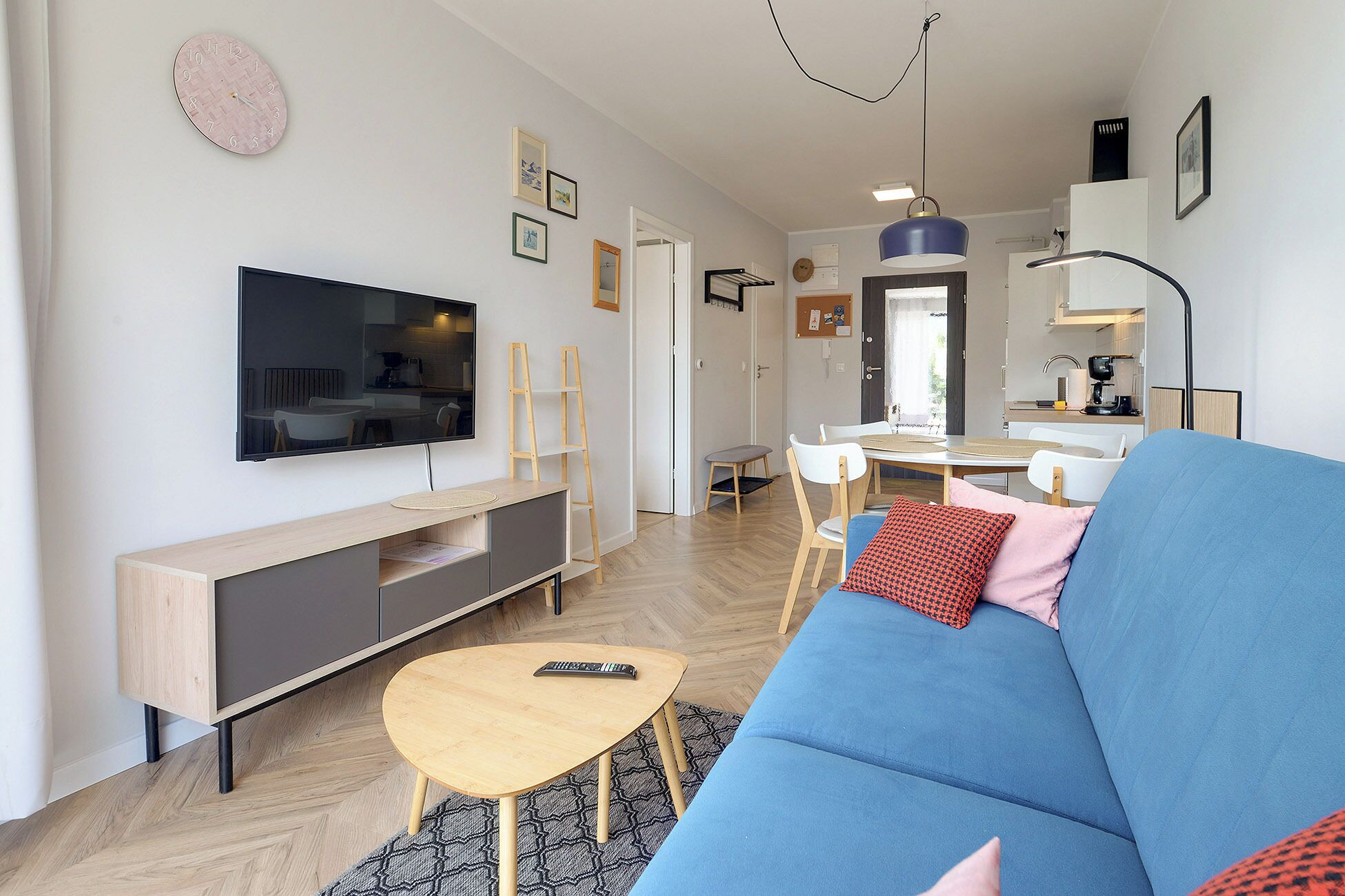 A modern living room with a large flat-screen TV, a blue sofa, a wooden coffee table, and a dining area with a small table and chairs.