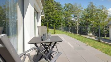 Een terras buiten met een tafel, stoelen, een glas water en uitzicht op een omheind tuintje.