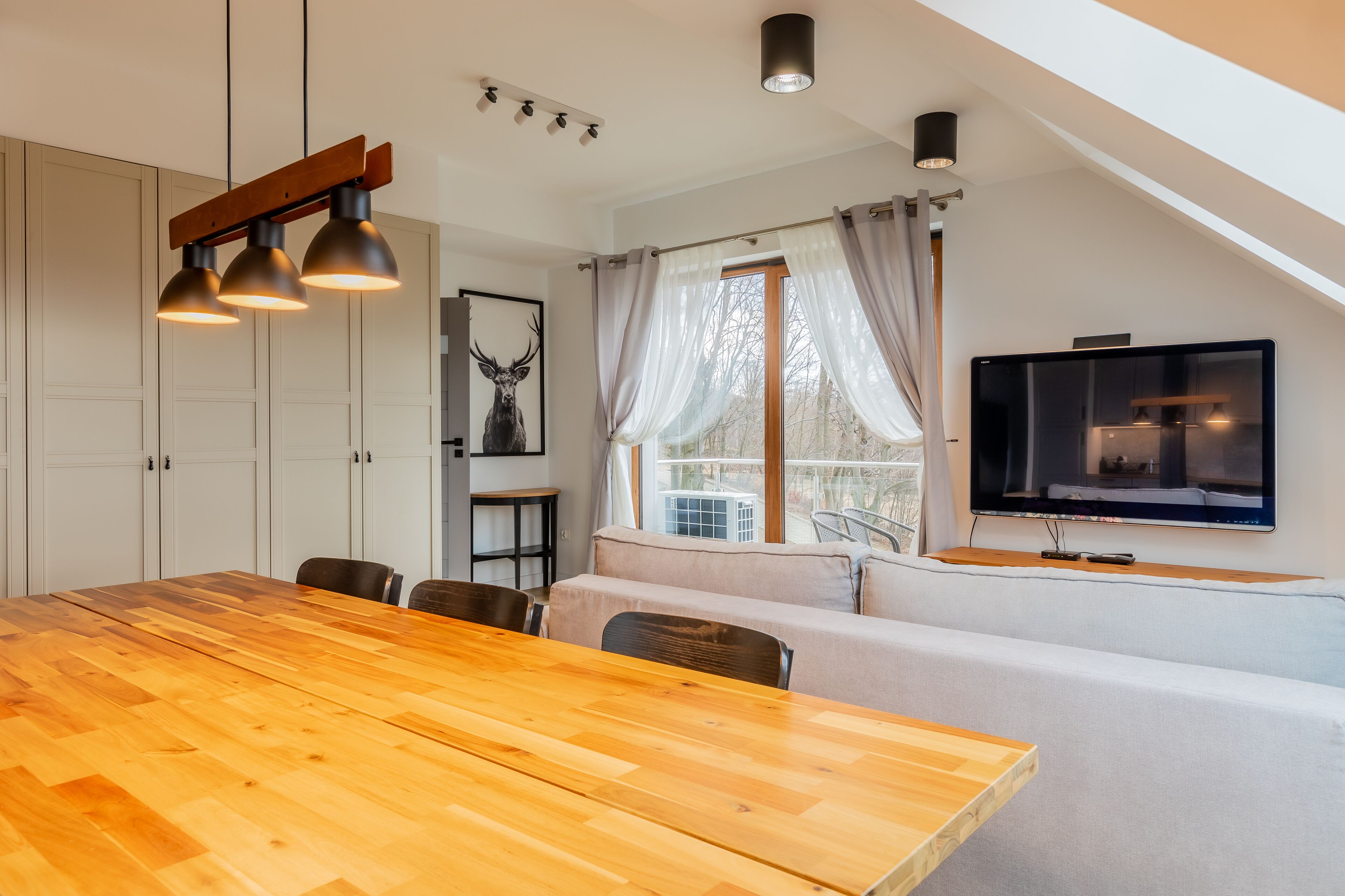 Une cuisine moderne avec une table à manger en bois, des meubles blancs et une grande fenêtre agrémentée de rideaux.