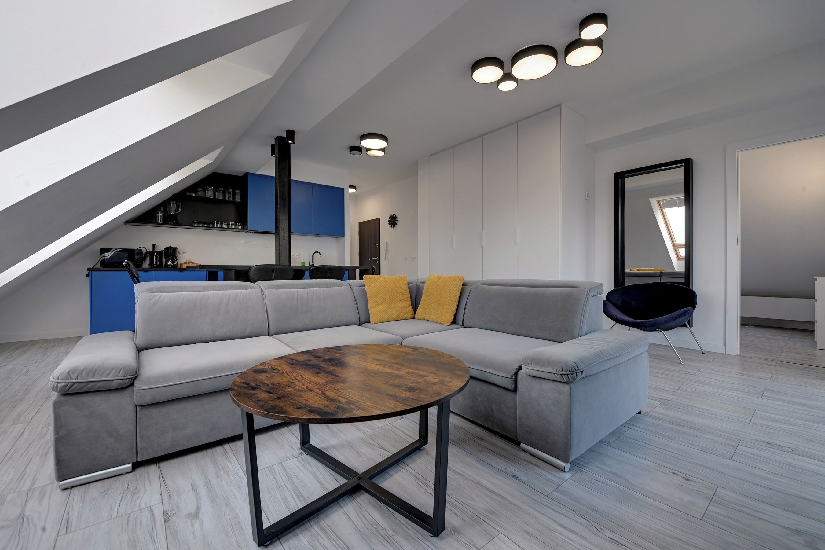 Un appartement moderne de style «loft» avec un canapé d’angle, une table basse ronde et une cuisine en arrière-plan.