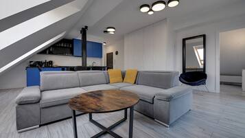Un appartement moderne de style «loft» avec un canapé d’angle, une table basse ronde et une cuisine en arrière-plan.