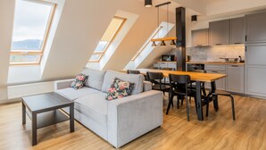 A modern loft apartment with a dining area, kitchen, and a gray sofa with floral cushions. - RentPlanet - Apartament Schroniskowa (Szklarska Poreba)