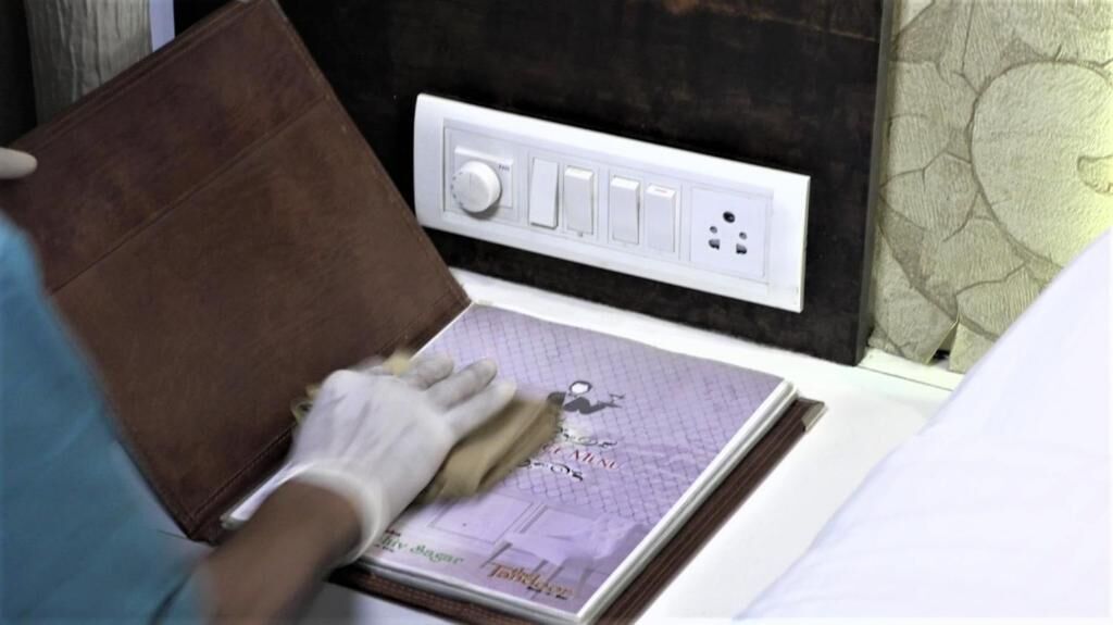 A person cleaning a leather sofa in a room with a white electrical outlet and a patterned wall.